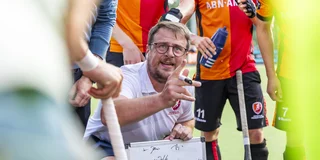 Coach Jeroen Baart met een whiteboard te midden van de cirkel tijdens een pauze.