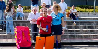 Nathalie en Emma Sophie Hessler staan lachend bij het hek langs het veld. Hun familie maakt foto's van de achterkant van hun shirts.